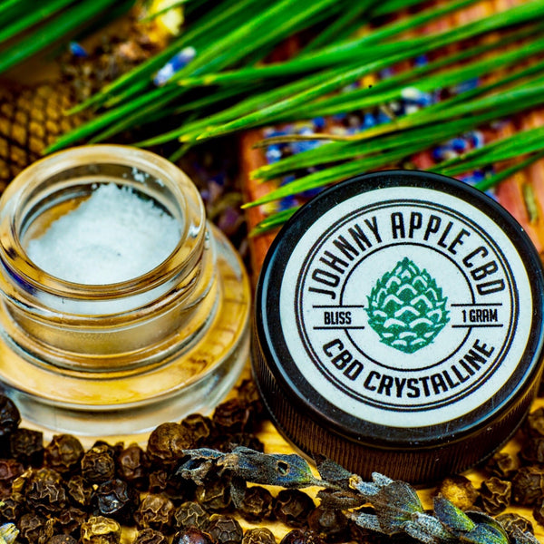 Johnny Apple CBD Bliss Hybrid crystalline jar beside an open jar of crystals, with lavender and black peppercorns